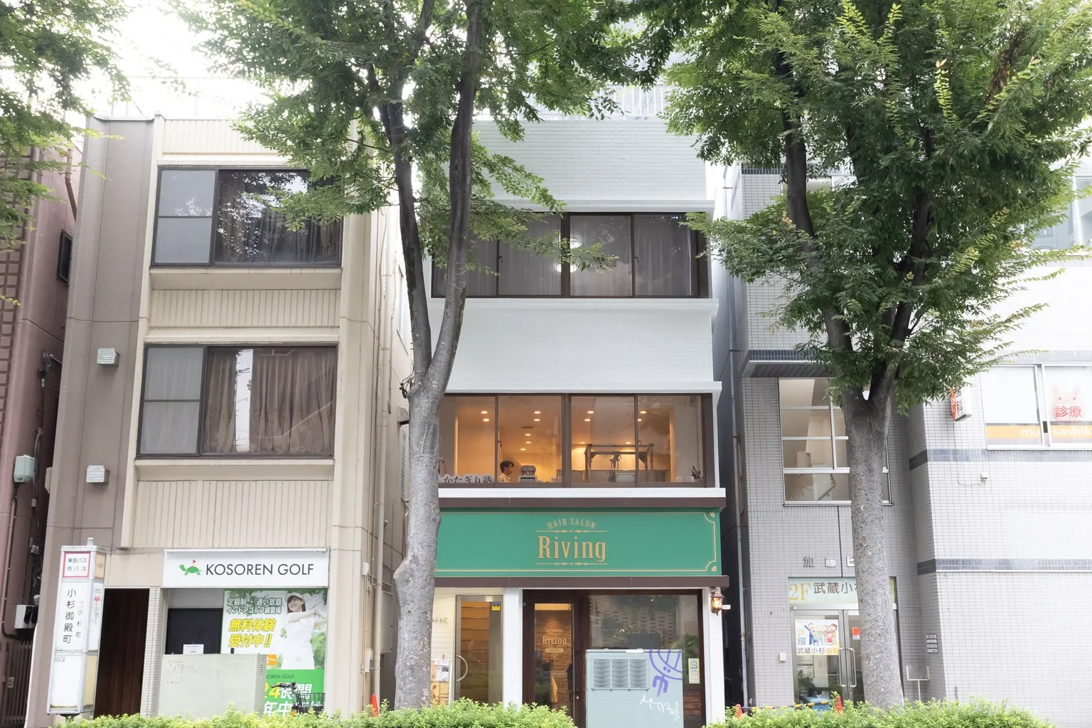 通りの向かいから見た、当院のある建物。1階に HAIR SALON Riving があり、建物の前に街路樹が並んでいる