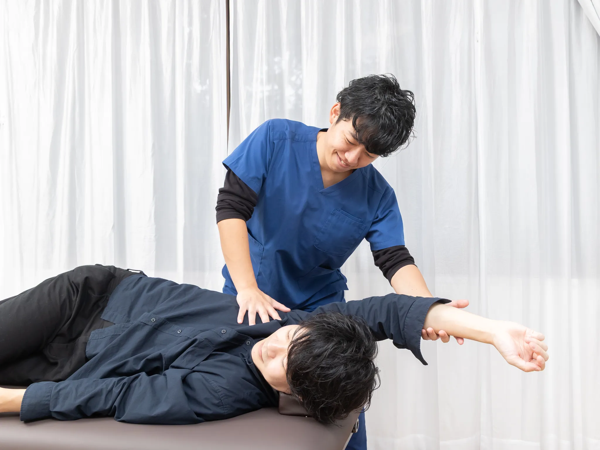 横向きに寝た方の背中に、施術者が手を当てている様子