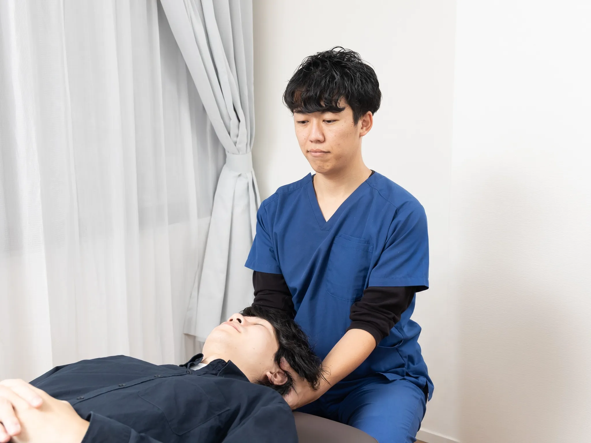 施術者が、仰向けに寝た方の首を両手で支えている様子
