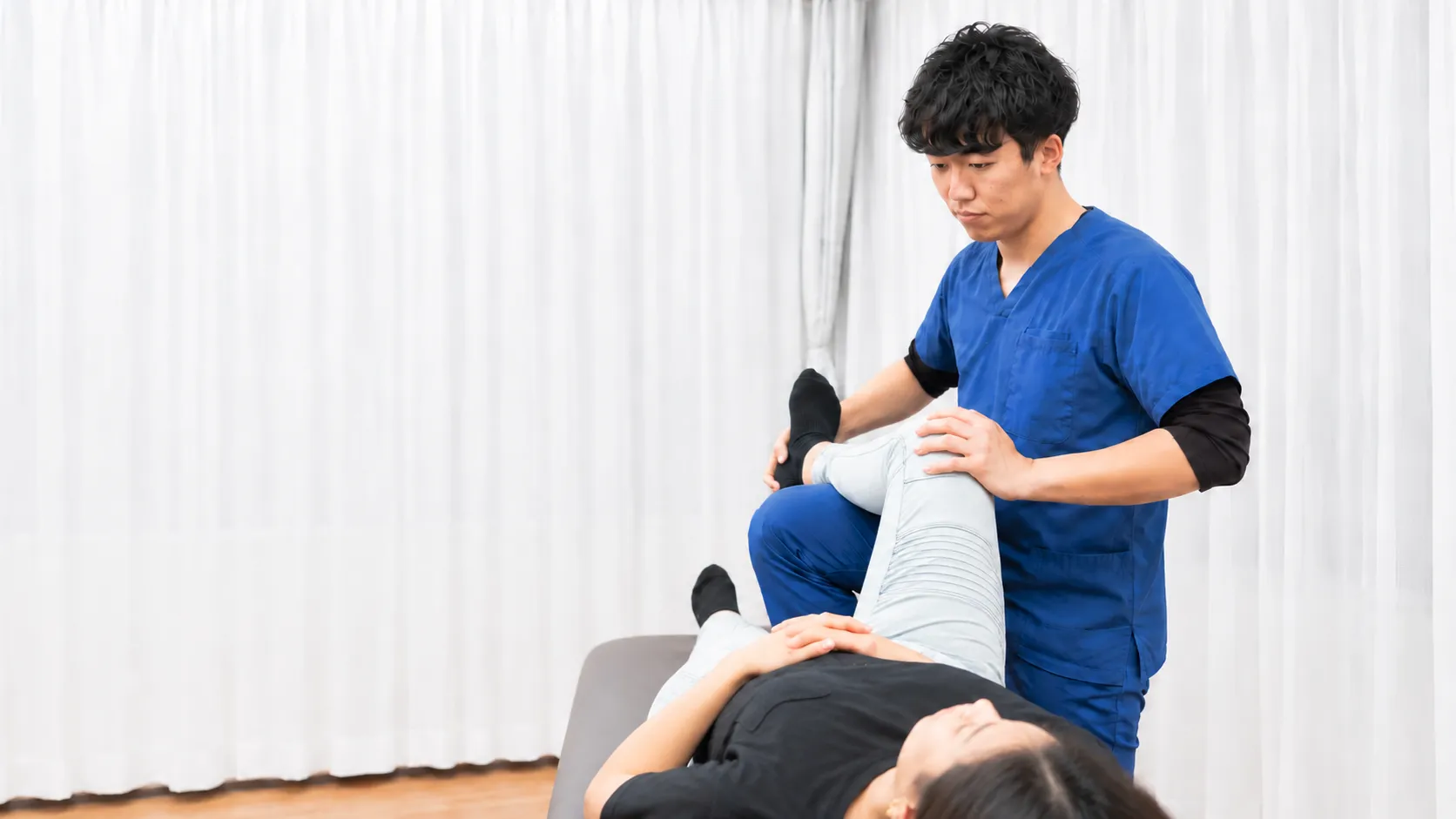 白い施術室で、施術者が仰向けの女性の脚を支えて施術している様子
